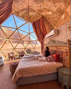 a woman sitting on top of a bed in a room filled with furniture and windows