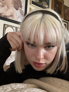 a woman with blonde hair and bangs laying on a bed in front of framed pictures