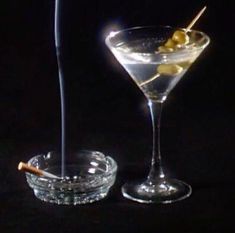 two martini glasses with olives in them on a black background, one is empty