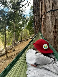 a person laying in a hammock with a red hat on and looking at the ground