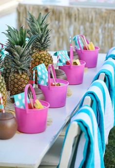 some pineapples are in pink buckets on a table with blue and white towels