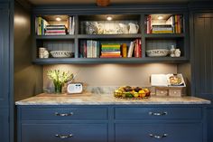 a kitchen with blue cabinets and marble counter tops, along with bookshelves full of books