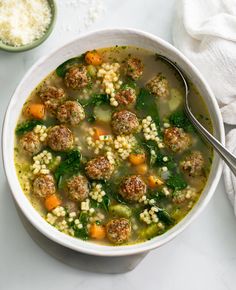 a white bowl filled with meatball soup next to a spoon and some rice on the side