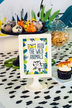 a table topped with cupcakes covered in frosting next to a sign that says don't feed the wild animals