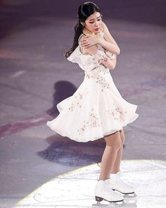 a woman in white skating on ice with her hands behind her head and arms around her neck