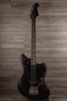 a black electric guitar sitting on top of a wooden floor next to a gray wall