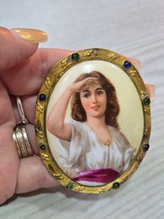 a woman's hand holding a ring with a painting on it