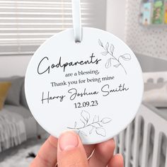 a person holding up a white ornament with the words godparents are a blessing thank you for being mine