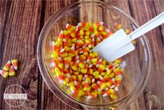 a glass bowl filled with candy corn on top of a wooden table