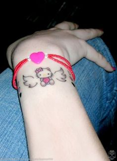 a person with a hello kitty tattoo on their arm holding onto a red string bracelet