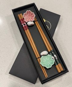 two chopsticks in a black box with some food on it and one has a pink flower