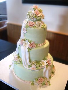 a three tiered green wedding cake with pink flowers on the top and white ribbon