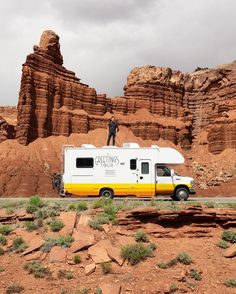 a man standing on top of a yellow and white camper van in the desert