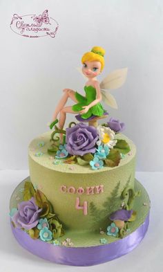 a cake decorated with flowers and a tinker fairy sitting on it's side