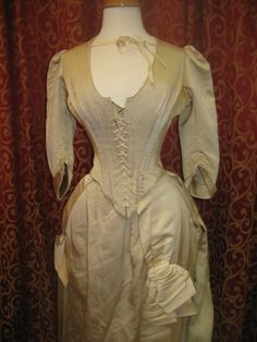 "1880's, 34\" bust, ecru silk faille, bustled and trained skirted wedding gown. A 19th century take on an 18th century lace up, low cut bodice. Bodice has a sharply pointed bottom, below waist, and 3/4 length cuffed sleeves. The bodice curves over hips, and is shorter in back than front. Bustled skirt has steel covered hoops built into back of skirt , and elaborate drapery forming into a long long train. Skirt has scalloped edge at bottom of the front, the bottom of train has a covered dust ruff Train Skirt, Bustle Skirt, Dust Ruffle, Long Train, Scalloped Edge, Cuff Sleeves, Wedding Gown, Low Cut, 18th Century