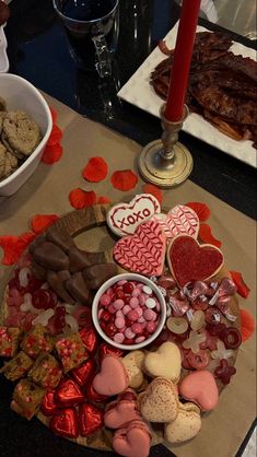 a table topped with lots of valentine's day food and desserts next to a lit candle