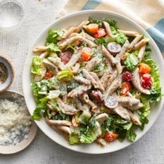 a white plate topped with pasta salad next to a bowl of dressing and spoons