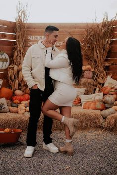 a man and woman standing next to each other in front of pumpkins