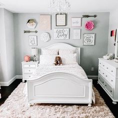 a white bed sitting under a chandelier in a bedroom next to a dresser