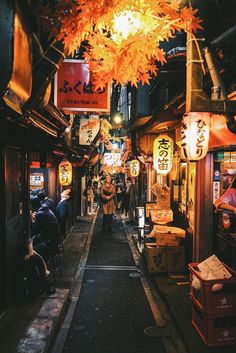 an alley way with people sitting at tables and signs hanging from the ceiling above it