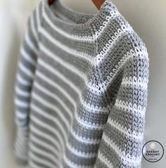 a gray and white striped sweater hanging on a wooden hanger next to a wall