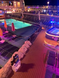 an empty swimming pool on the deck of a cruise ship at night with umbrellas and chairs