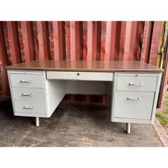 an old metal desk with two drawers in front of a red shipping container on the ground