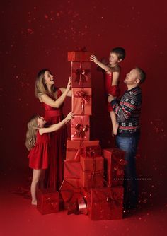 a family with two children standing next to a stack of wrapped presents on a red background