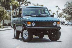 a blue land rover is parked on the side of the road in front of palm trees