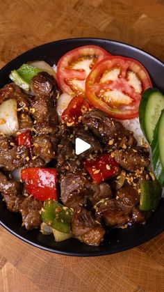 a black plate topped with meat and veggies on top of a wooden table