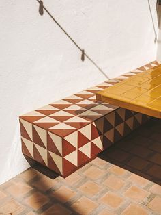 a yellow and brown bench sitting on top of a brick floor next to a white wall