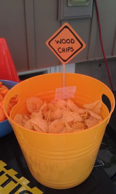 a yellow bucket filled with chips sitting on top of a table next to a sign that says wood chips