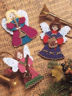 three christmas angel ornaments on top of sheet music with trumpet and pine tree in foreground