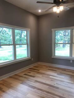 an empty room with two windows and a ceiling fan in the middle of the room