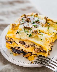 a white plate topped with lasagna covered in cheese and mushrooms next to a fork