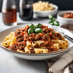 a white plate topped with pasta covered in meat sauce and garnished with basil