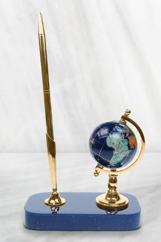 a pen is sitting on top of a blue stand with a globe and gold trimming