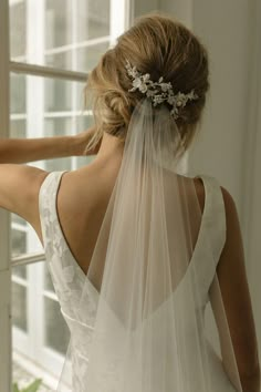 the back of a bride's wedding dress with a veil on her head and flowers in her hair