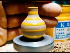 a person holding a yellow and white vase next to some jars on the ground with their hands