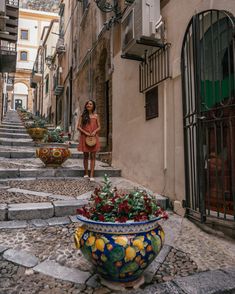 a woman is walking down the street in an alleyway with flowers and potted plants