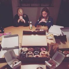 two people sitting at a table with boxes of doughnuts