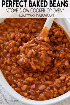 a white bowl filled with baked beans sitting on top of a counter next to a wooden spoon