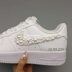 a woman's hand holding up a white nike air force with pearls on it