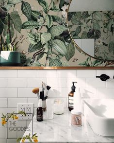 a bathroom counter with soap, lotion bottles and flowers on the wall behind it