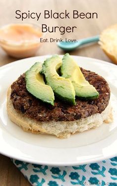 a burger with an avocado on top sits on a white plate next to some bread