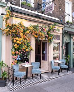 the outside of a restaurant with flowers on the wall and chairs in front of it