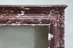 an old red frame with white paint on the top and bottom part of it, sitting in front of a gray wall