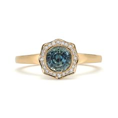 a ring with an oval blue diamond surrounded by small white diamonds in the center, on top of a plain yellow gold band