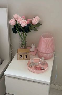 a white table topped with pink flowers next to a clock and vase filled with roses