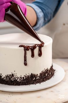 someone is decorating a white cake with chocolate icing and sprinkles